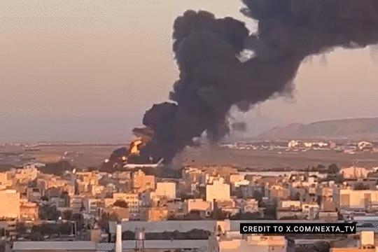 Large plume of black smoke rising over a city.