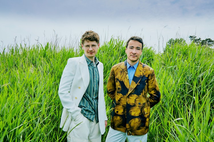 Pavel Kolesnikov and Samson Tsoy standing in tall grass.