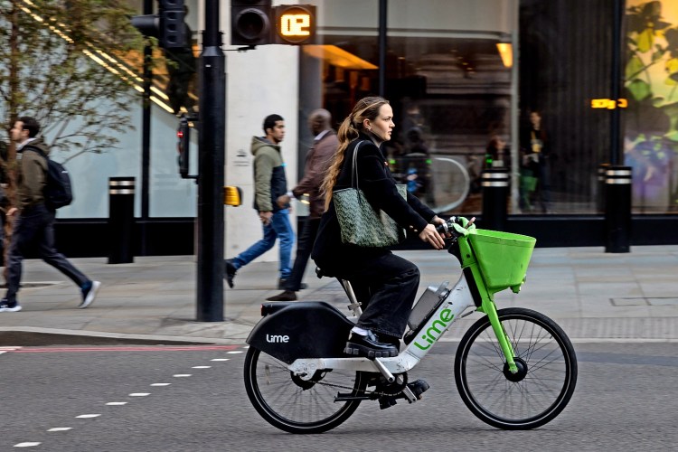 Woman riding a Lime electric bike through a pedestrian crossing.