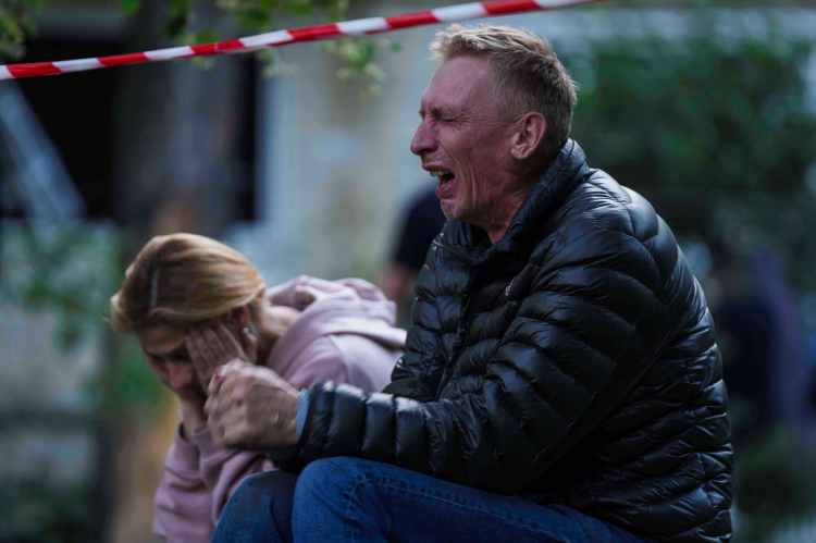 A grieving father cries while his son is trapped under rubble from a destroyed building.