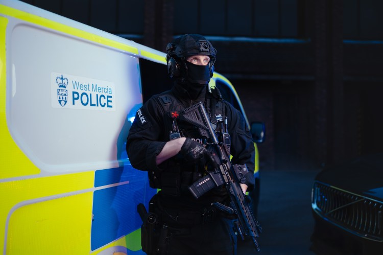 Armed response officer standing by a police van.