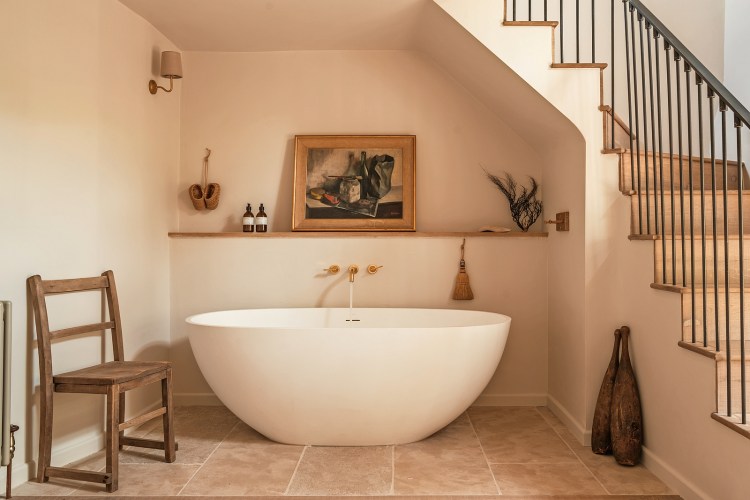 Freestanding bathtub in a minimalist bathroom with a wooden shelf above it.