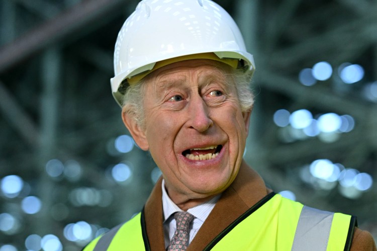 King Charles III wearing a hard hat and safety vest at a wind turbine factory.