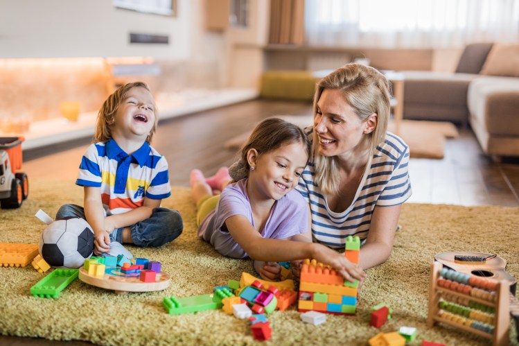 A single mother playing with her two children on the floor.