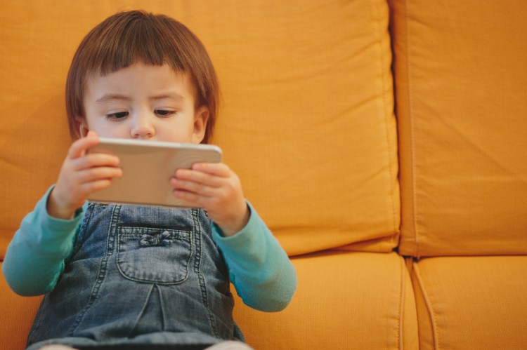 Toddler using a smartphone on a couch.