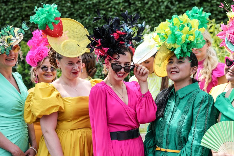 Women in colorful dresses and elaborate hats at Ascot race course.