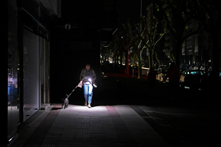 Woman walking dog at night using phone as flashlight during power outage.
