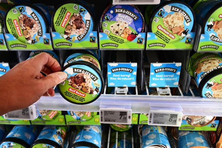 A hand selecting a pint of Ben & Jerry's Half Baked ice cream from a freezer.