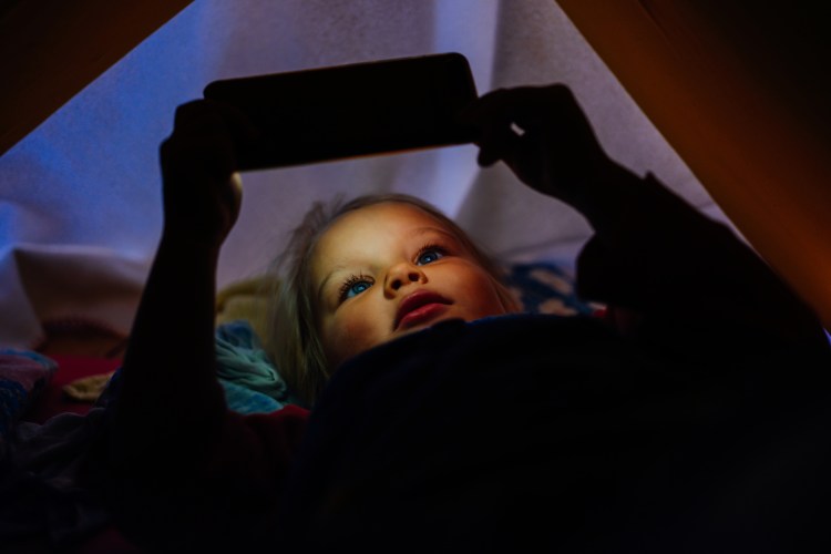 Toddler lying in bed watching a video on a phone.