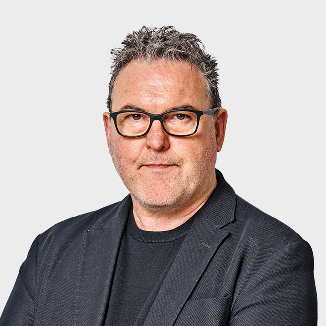 a man wearing glasses and a black jacket looks at the camera