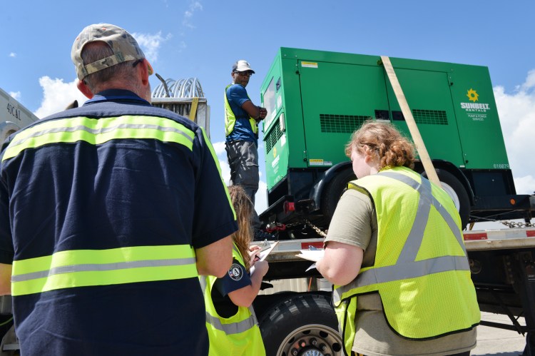 People inspecting a Sunbelt Rentals generator on a flatbed truck.