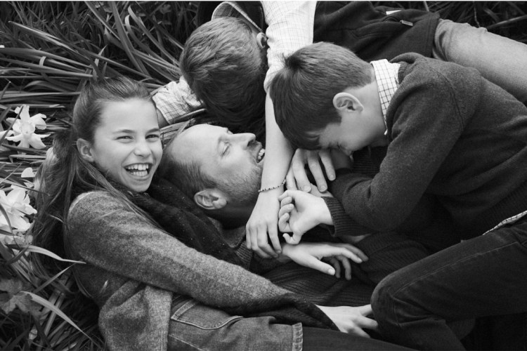 Black and white photo of a father lying on the ground surrounded by his three children.