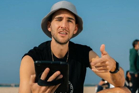 Man crouching on beach, holding tablet and gesturing.
