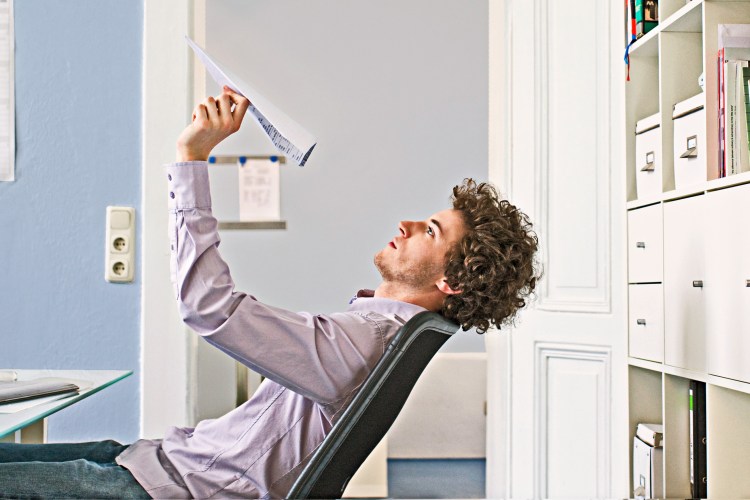 Businessman leaning back in his chair, launching a paper airplane.
