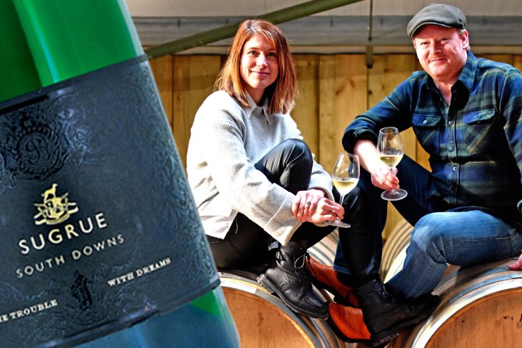 A couple sits on wine barrels, tasting wine; a bottle of Sugrue South Downs wine is featured.