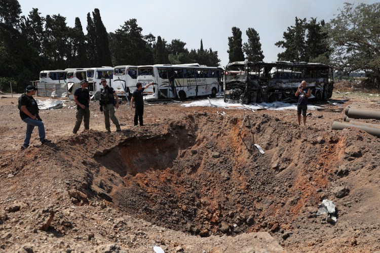 Police officers examine a crater near damaged buses after a missile attack in Herzliya, Israel.