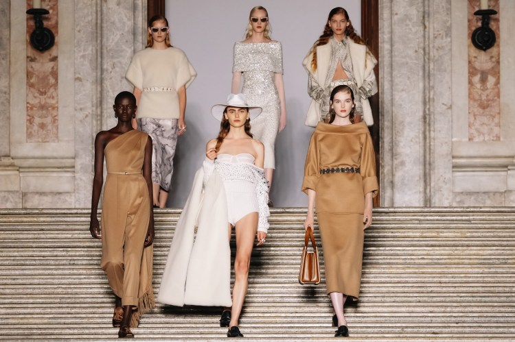 Models walking down stairs in beige and white outfits at the Max Mara Cruise fashion show.