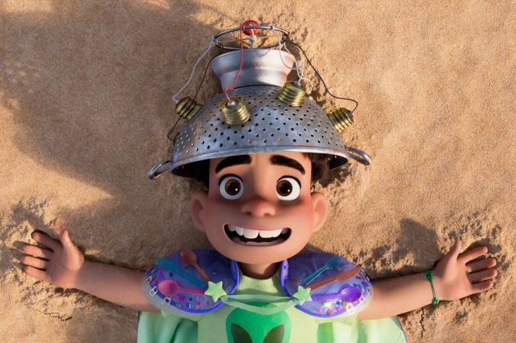 Film still of Elio, a boy wearing a colander on his head, lying on the sand.